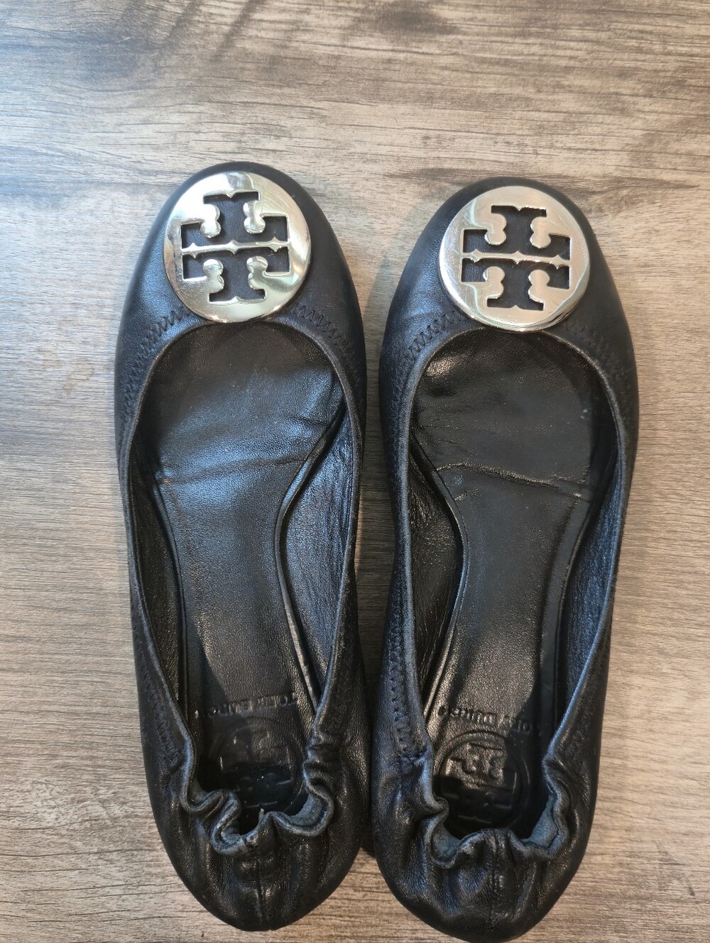 These are Tory Burch Reva ballet flats in black leather with a prominent silver